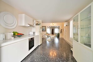 Eine moderne Küche mit weißen Schränken, einem schwarzen, gefleckten Boden und einem Essbereich mit weißen Stühlen und einem Tisch.