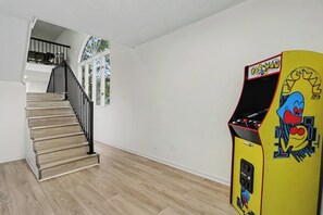 A staircase with a black railing leading to a landing, a yellow arcade machine with a Pac-Man design, and a wooden floor.