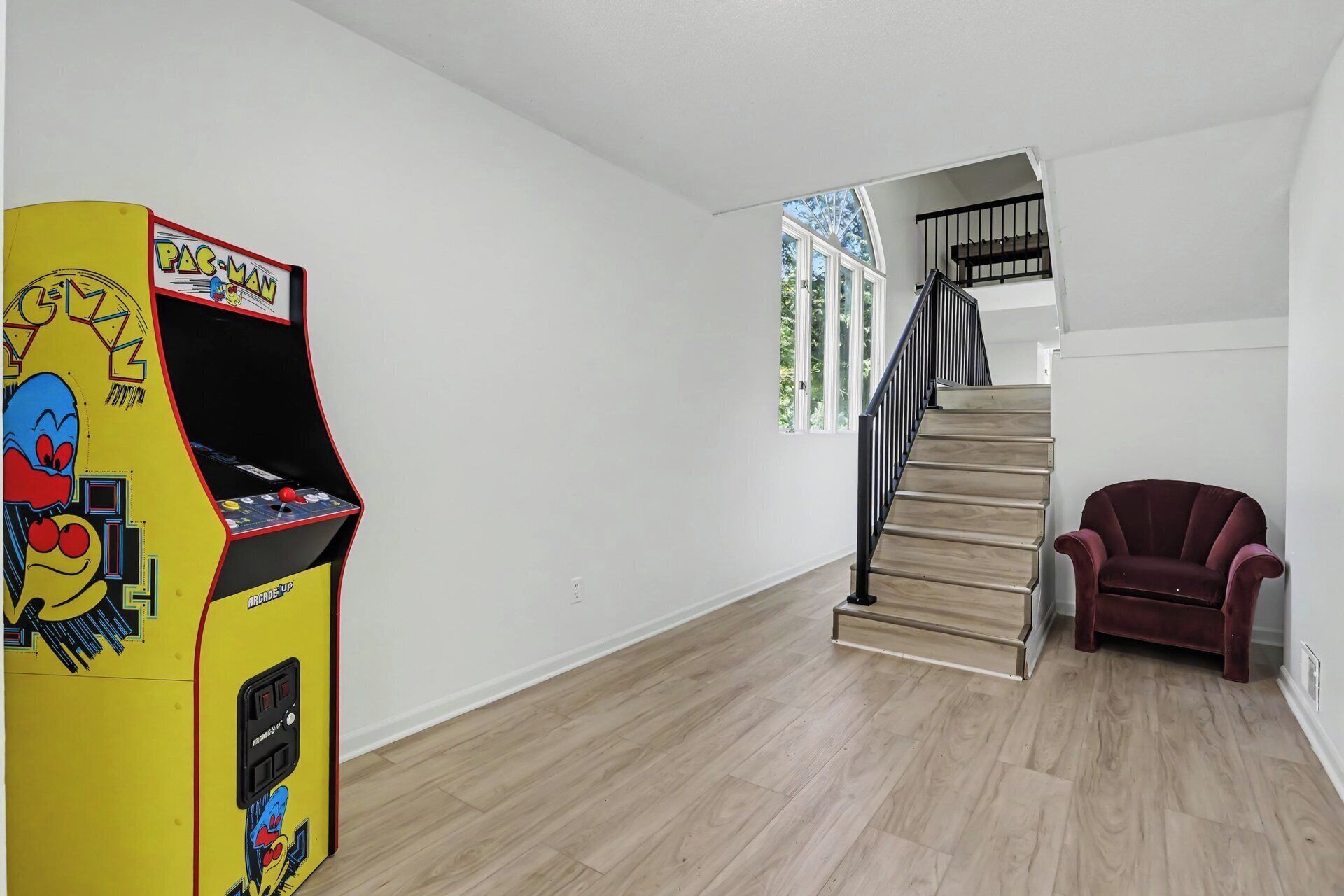 Une pièce avec une borne d’arcade Pac-Man, un escalier et un fauteuil rouge.