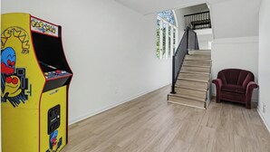 A room with a wooden floor, a staircase, a red chair, and a Pac-Man arcade machine.