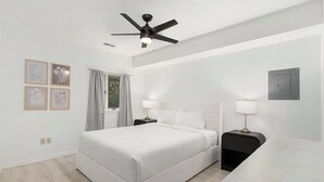Ein modernes Hotelzimmer mit einem großen Bett, Nachttischen, einem Deckenventilator und gerahmten Kunstwerken an der Wand.