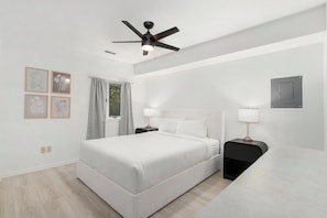 Ein modernes Hotelzimmer mit einem großen Bett, Nachttischen, einem Deckenventilator und gerahmten Kunstwerken an der Wand.