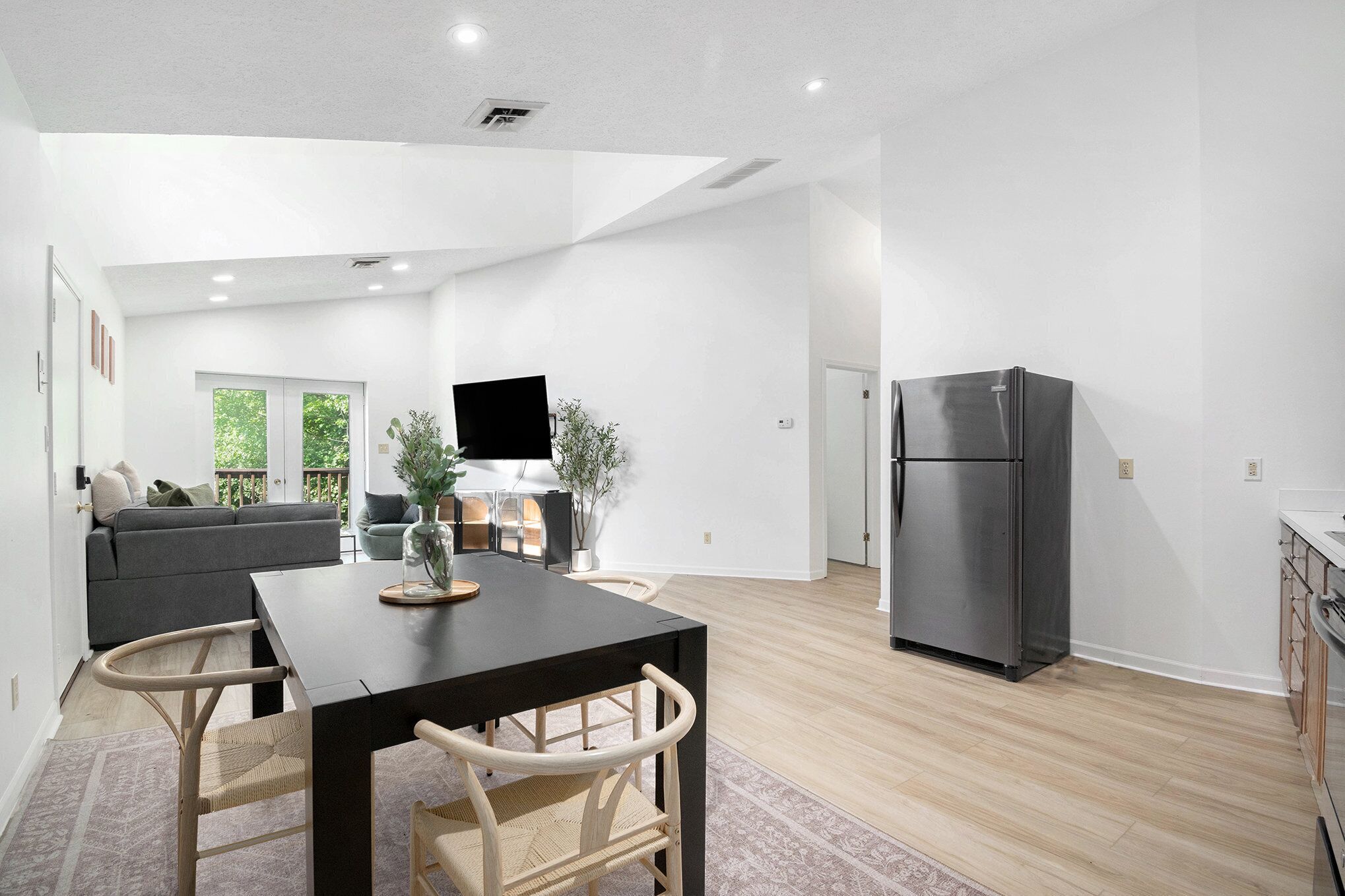 A modern kitchen with a built-in refrigerator, a dining area with a table and chairs, and a living area with a sofa and a television.