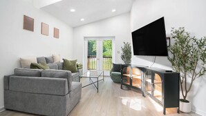 Ein modernes Wohnzimmer mit einer grauen Sofagarnitur, einem Glastisch, einer schwarzen Unterhaltungsanlage und einem großen Fernseher.