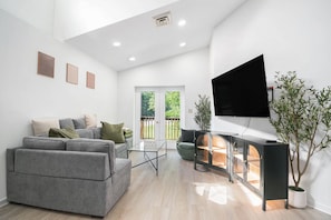 Ein modernes Wohnzimmer mit einer grauen Sofagarnitur, einem Glastisch, einer schwarzen Unterhaltungsanlage und einem großen Fernseher.