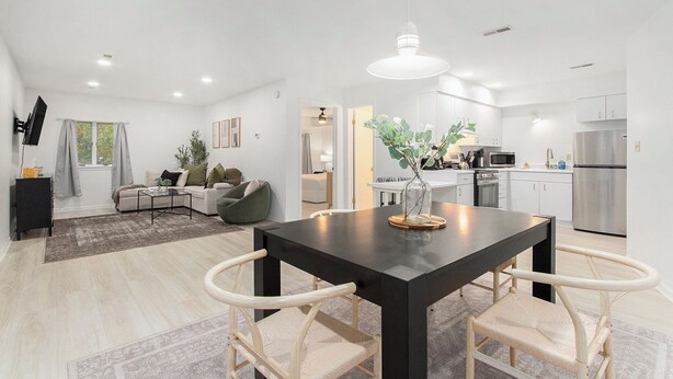 Eine moderne Küche mit Edelstahlgeräten, ein Essbereich mit einem schwarzen Tisch und weißen Stühlen sowie ein Wohnzimmer mit einer Couch und einem Couchtisch.