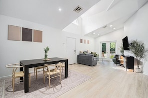 A modern interior with a dining area, sofa, TV, and a plant. - Lake-Vibes Retreat | Beaches | Wineries (Sawyer)