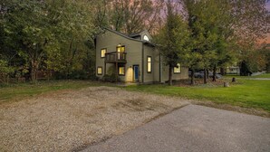 A two-story house with a balcony, surrounded by trees and a gravel driveway. - Lake-View Hideaway | Beaches | Wineries (Sawyer)
