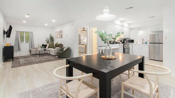 A modern living room with a dark wooden dining table, white wicker chairs, a black sofa, and a grey rug. - Lake-View Hideaway | Beaches | Wineries (Sawyer)