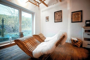 A room with wooden flooring, a large window, two wooden chairs, a white furry rug, and a small wooden cabinet. - Thatched cottage with private dike on the Elbe (Freiburg Elbe)