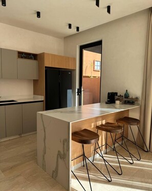 A modern kitchen with a marble island, wooden stools, and a black refrigerator. - Villa Camelia - Breakfast and Heated Pool (Marrakech)