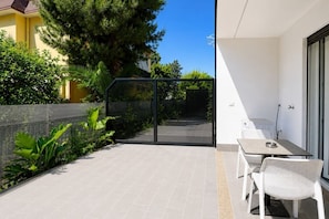 Ein Balkon mit Tisch und Stühlen, eine Glastür und Blick auf eine Straße sowie Grünflächen.