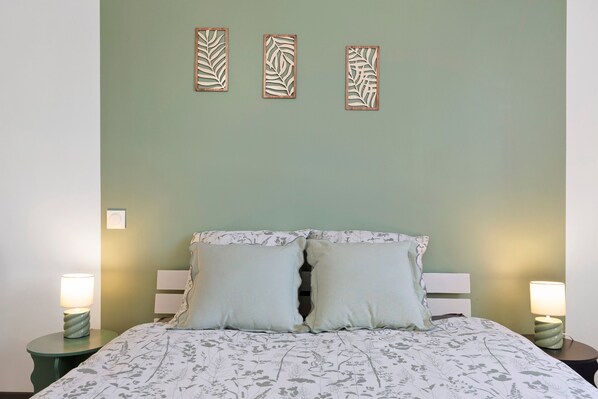 Una cama con ropa de cama floral, dos lámparas de noche y tres paneles decorativos en la pared.