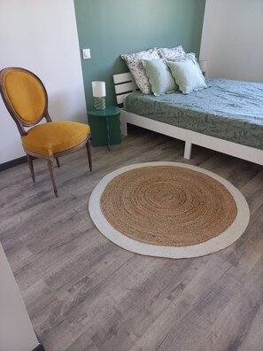 A bedroom with a bed, a chair, a bedside table, and a round rug.