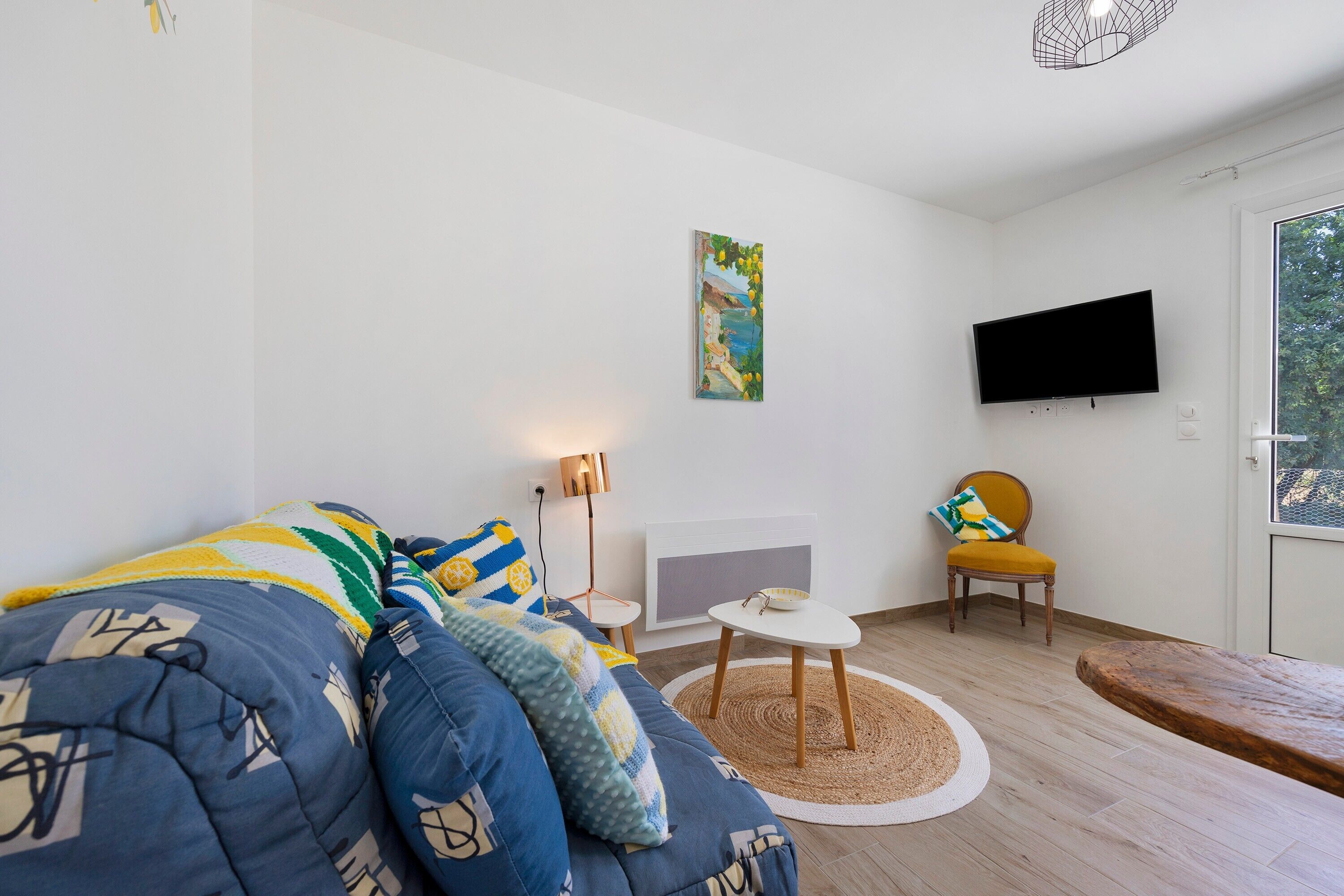 Een moderne woonkamer met een bank, een fauteuil, een salontafel, een televisie en een schilderij aan de muur.