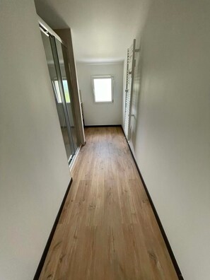 Un couloir étroit au plancher en bois, avec une fenêtre au fond et une porte sur le côté gauche.