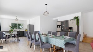 A modern dining area with a table set for six, surrounded by grey upholstered chairs, a kitchen in the background, and a staircase leading to an upper level. - Holiday Home “L'Or du Temps” with Private Terrace, Garden and Wi-Fi (Froidfond)