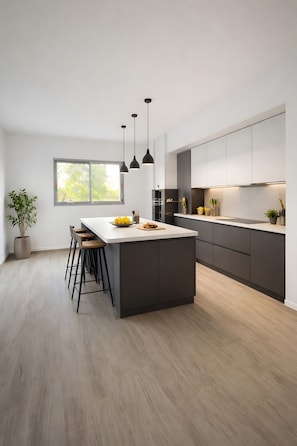 Une cuisine moderne dotée d’un îlot central, de tabourets de bar, de luminaires suspendus et d’une grande fenêtre.