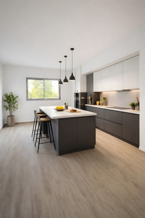 A modern kitchen with a central island, bar stools, pendant lighting, and a large window.