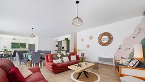 A modern living room with a red sofa, a coffee table, and a dining area with a table and chairs. - Holiday Home “L'Or du Temps” with Private Terrace, Garden and Wi-Fi (Froidfond)
