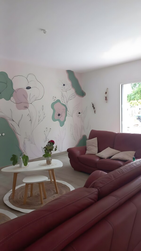 Un salon moderne avec un canapé rouge, une table ronde en bois et une fresque murale.