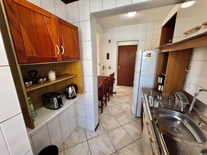 A kitchen with wooden cabinets, a refrigerator, a sink, and a dining area with chairs. - Unleash your best self by the sea! (Florianópolis)