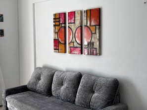 Ein graues Sofa vor einer weißen Wand mit drei abstrakten Gemälden.