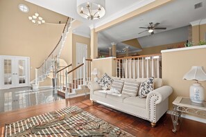 A spacious living room with a high ceiling, a staircase, a sofa with decorative pillows, a chandelier, and a floor lamp. - West Austin Retreat, Hill Views, Fireplace & Near Downtown (Austin)