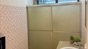 Un baño con cabina de ducha, lavamanos y una pequeña planta en maceta.