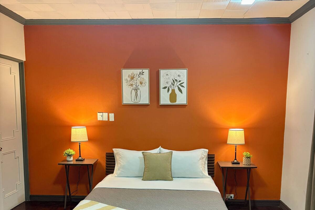 A hotel room with a bed, two bedside tables with lamps, a decorative wall, and a wooden floor.
