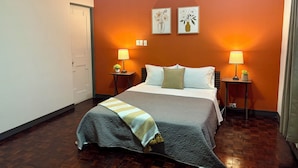 Una habitación de hotel con una cama, dos lámparas de noche, una mesita de noche, una puerta y dos cuadros colgados en la pared.