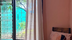 Una habitación con ventana, una silla con cojín y suelo de madera.