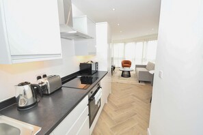 A modern kitchen with a toaster, kettle, and oven, a dining area with a table and chairs, and a living room with a sofa and a chair. - Modern & Bright 1BED Apartment in Leeds - Sleeps 3 (Leeds)