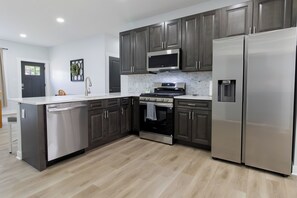 A modern kitchen with dark cabinets, stainless steel appliances, and a tiled backsplash. - Entire Home In Miller close to BP/80/94 (Gary)