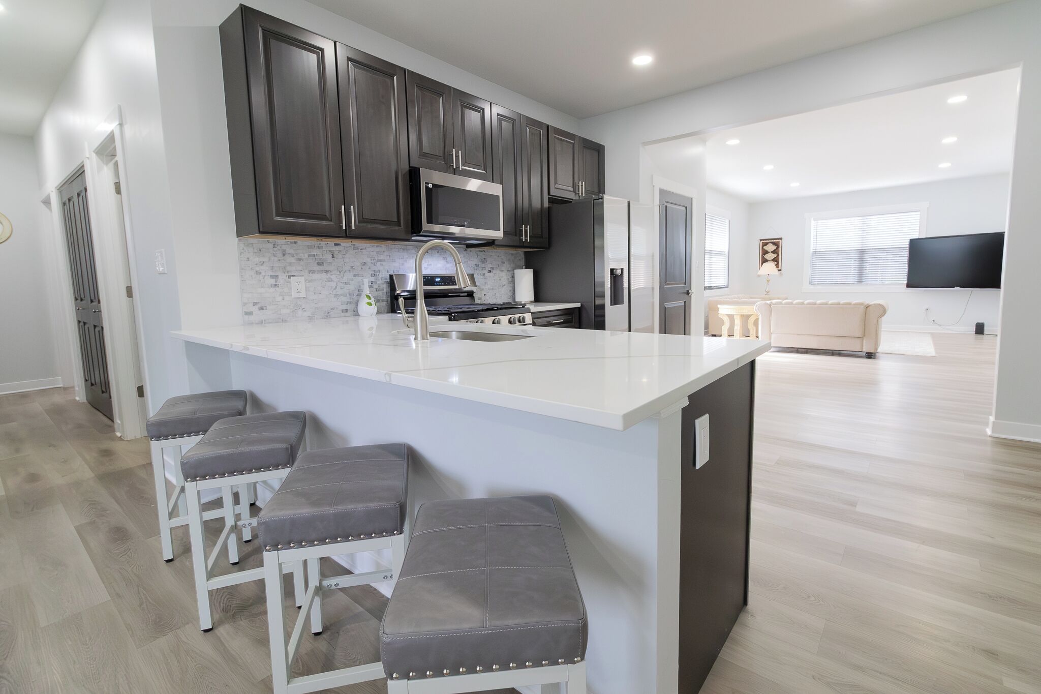 A modern kitchen with dark cabinets, a large island with bar stools, a microwave, stove, and refrigerator.