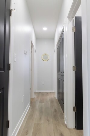 A hallway with white walls, a wooden floor, and a door with a black frame. - Entire Home In Miller close to BP/80/94 (Gary)