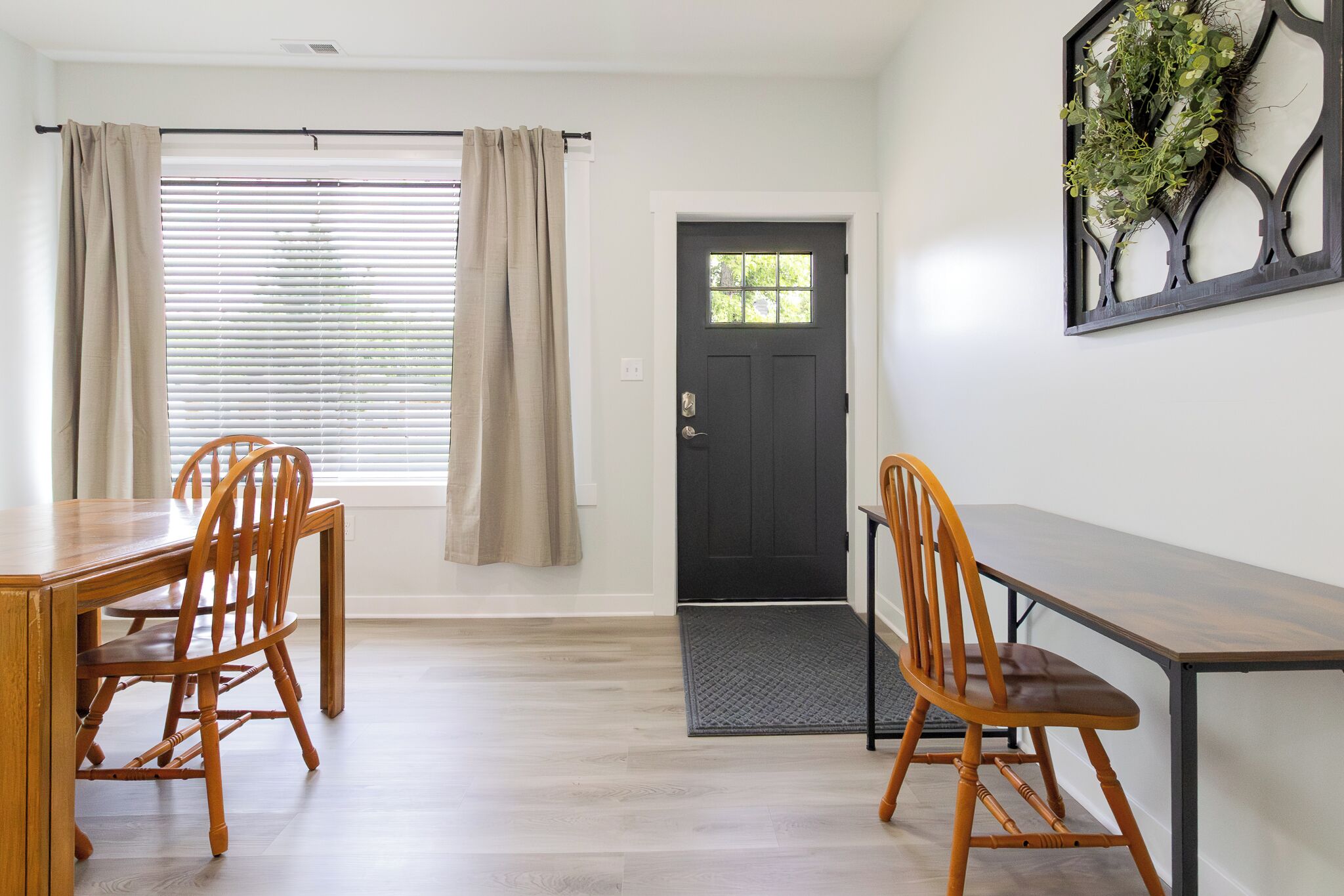 A dining area with a wooden table and chairs, a black door, and a window with blinds.