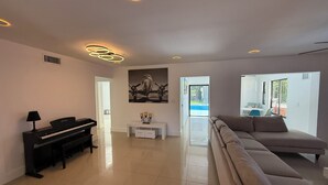 Una sala de estar moderna con un piano, un sofá, un comedor y vistas al exterior.