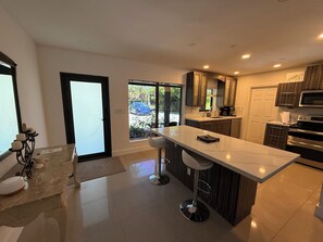 A modern kitchen with a large island, dark wood cabinets, stainless steel appliances, and a sliding glass door leading to a patio. - Beautiful Oasis Private Pool (Plantation)