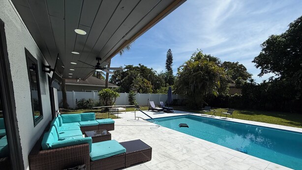 Una piscina con un sillón de sol y una zona de estar techada.