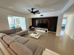 A modern living room with a sectional sofa, a flat-screen TV, a ceiling fan, and a large window. - Beautiful Oasis Private Pool (Plantation)