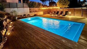 En rektangulär swimmingpool med en träbrygga runt om, omgiven av en låg stenmur och ett trästaket.