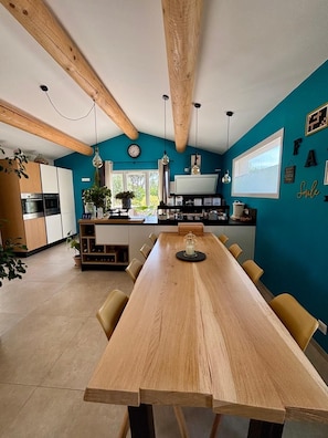 Eine moderne Küche mit Holzbalken, einem Essbereich mit einem langen Tisch und einer Wand in Türkisblau.