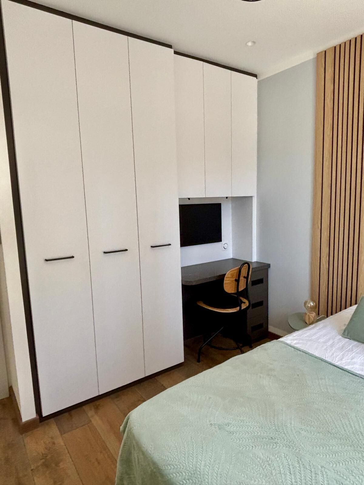 A bedroom with a bed, a desk with a chair, a wardrobe, and a television.
