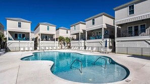 A pool area with a curved pool, lounge chairs, and a clear blue sky. - DJs Coastal Retreat in Gulf Shores, AL (Gulf Shores)