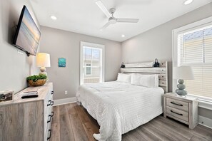 A bedroom with a bed, bedside tables, a TV, and a ceiling fan. - DJs Coastal Retreat in Gulf Shores, AL (Gulf Shores)