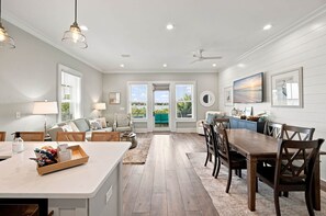 A spacious living area with a dining table, sofas, and a view through the glass doors. - DJs Coastal Retreat in Gulf Shores, AL (Gulf Shores)