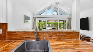 Une cuisine moderne dotée d’un grand évier, d’un plancher en bois et offrant une vue sur une piscine et sur la verdure.