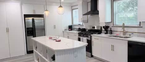 A modern kitchen with white cabinetry, a central island, stainless steel appliances, and pendant lighting.