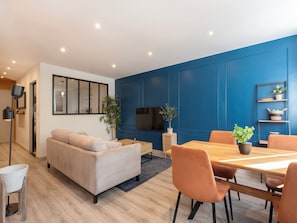 Un salon moderne avec un canapé, une table à manger, des chaises, un téléviseur et un mur d’accent bleu.